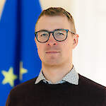 A man in 30s with short light hair and round glasses.