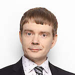 The photo shows a young man with short reddish-brown hair, wearing a tie and a black suit. The photo is three years old; in real life, he is slightly older now, has gained a few kilos, and has some grey at his temples. He looks directly at the camera with a slight smile, as if trying to see through the screen or printed page to connect with the viewer or reader.